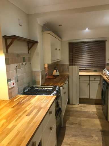 Bright kitchen with wooden countertops, cream cabinets, and a window with wooden blinds.