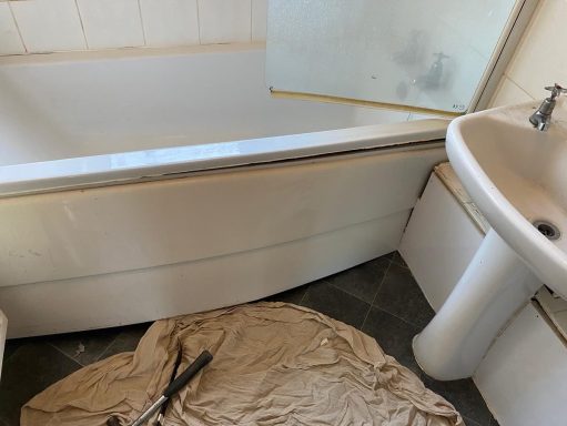 Bathroom interior featuring a bath, sink, and a cloth on the floor.